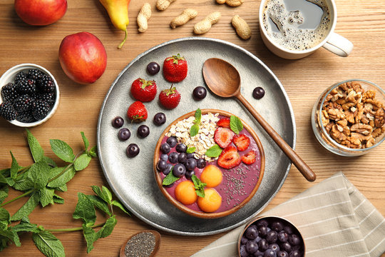 Flat lay composition with bowl of tasty acai smoothie and ingredients on wooden table