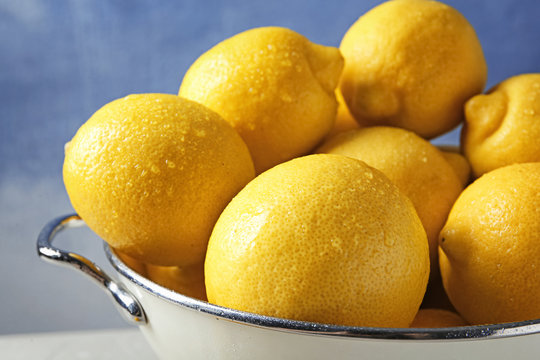 Colander with ripe lemons against color background