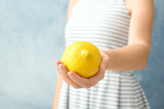 Woman holding ripe lemon against color background, closeup