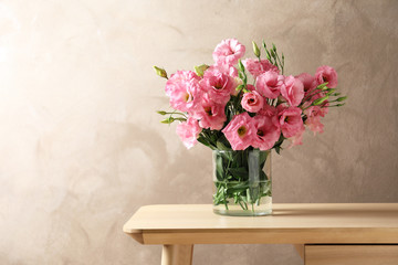 Vase with beautiful Eustoma flowers on table against color background