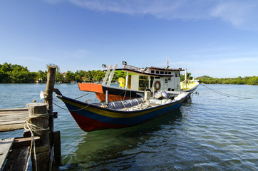 Naklejka na ściany i meble traditional malaysian fisherman boat moored near the riverbank over blue sky background