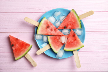 Flat lay composition with watermelon popsicles and ice cubes on wooden background