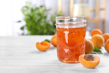 Jar with tasty apricot jam on table