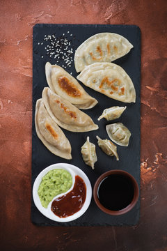 Different types of fried korean dumplings with dipping sauces on stone slate, flatlay on a fire-warm rusty metal background