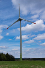Windkraftanlage auf einer Wiese vor blauen Himmel mit wei&szlig;en Wolken