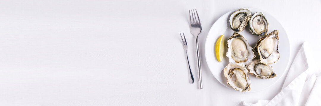 Top view of Fresh oysters served in white plate with sliced of lemon on white tablecloth. With copy space.