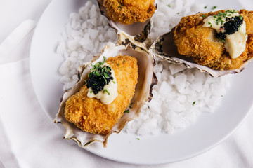 Close up of Deep fried oysters topping with mayonnaise and caviar served in white plate with sea salt decorated.