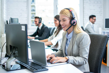 Portrait of beautiful blonde female customer service executive with headset using laptop in office