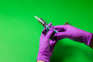Hands In Pink Rubber Gloves Hold A Blue Tattoo Machine On A Green Background