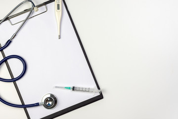 Stethoscope, syringe and thermometer on clipboard with blank paper