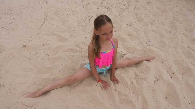 Young girl doing splits and stretching on sandy beach, overhead view
