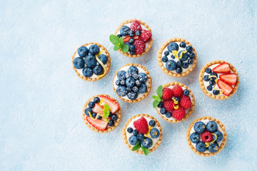 Table bleue décorée de sucre en poudre avec variété de tartelettes aux baies ou vue de dessus de gâteau. Desserts pâtissiers savoureux.