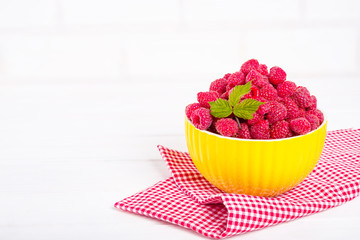Fresh raspberry in a modern yellow bowl on light background