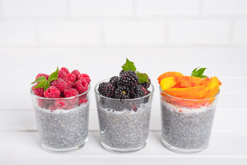Healthy eating and dieting concept. Chia pudding with fresh berries and green leaves for breakfast on a light kitchen table. Three glasses, raspberry, blackberry, apricot or peach. Copy space.