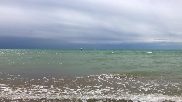 View of sea line with windsurfer far away, soft aquamarine waves and dark cloudy low sky