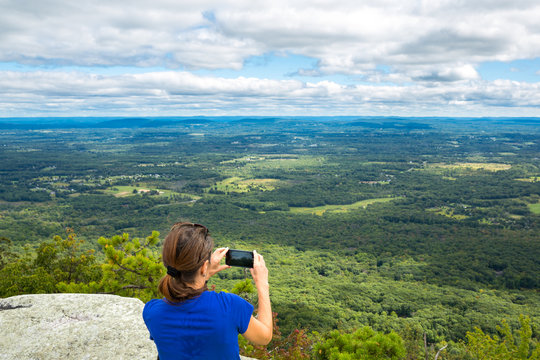 Woman takes a snpashot of the Hudson Valley farm land from Gertrude's Nose hiking trail, in Upstate New York