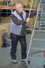 senior worker with white helmet looking up in warehouse