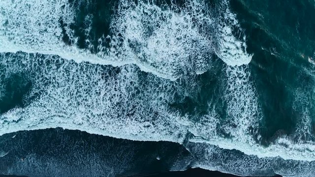 Strong waves on the evening beach with black sand in Indonesia, Bali. Aerial view. 4K