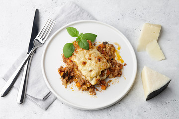 Traditional meat lasagna with minced beef, bolognese and bechamel sauce in white round plate on grey stone background