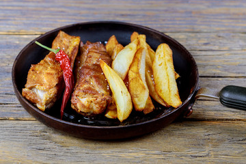 Fried pork ribs in frying pan, and with potatoes close up.