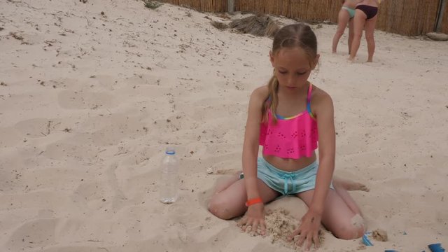 Adorable female child playing with sand and sitting on beach