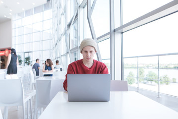 Stylish student in casual clothing sitting in a light cafe and using a laptop. Portrait of a freelancer working in a light restaurant on a laptop.