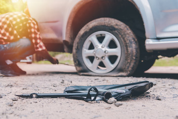 Young man is changing tires on car the road because he was repairing in the bright sunlight.