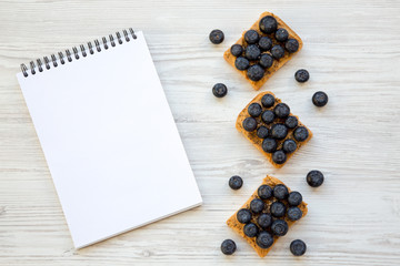 Vegan toasts with peanut butter, blueberries and chia seeds on a white wooden background, top view. Healthy eating. Flat lay, from above. Blank notebook.