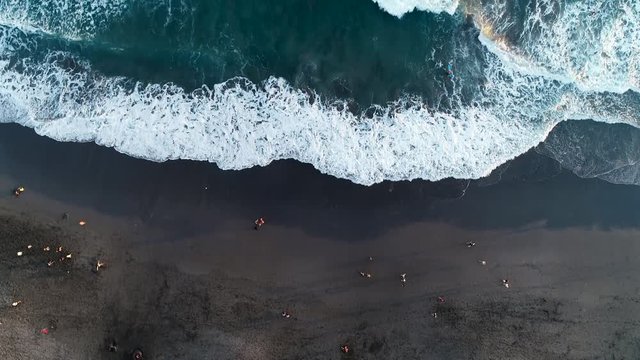 Strong waves on the evening beach with black sand in Indonesia, Bali. Aerial view. 4K