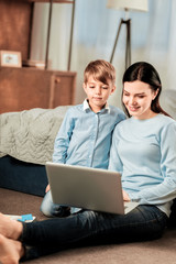 Modern technology. Joyful nice woman holding a laptop while being together with her son