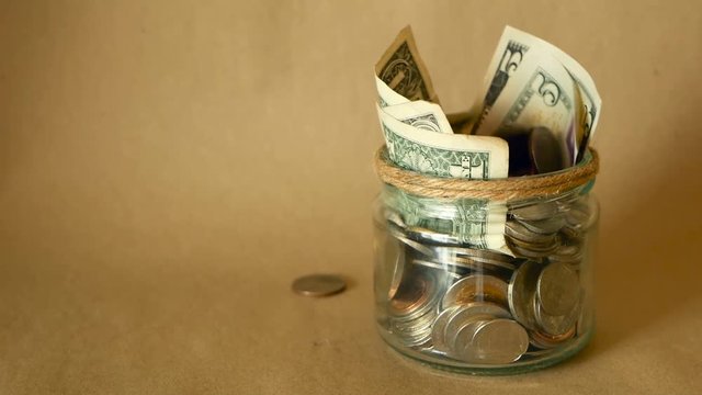 Saving money coin in jar. Symbol of investing, keeping money concept. Collecting cash banknotes in glass tin as moneybox. American dollars close-up vintage tone background. Piggy bank in a glass jar