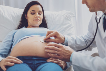 Fototapeta premium Keep attention. Pleased pregnancy demonstrating her belly while communicating with doctor