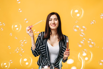 Young woman blows soap bubble, yellow background