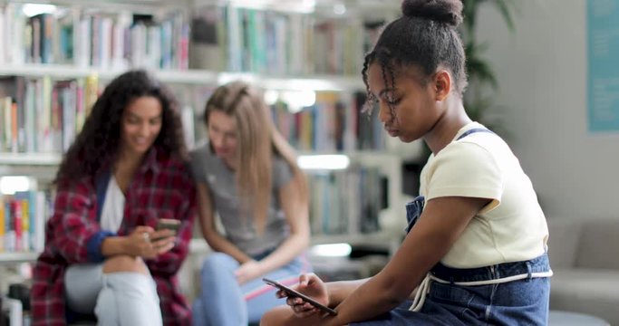 Student alone using smartphone at recess in library