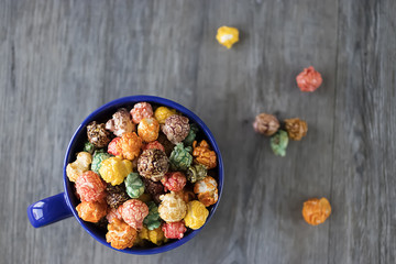Multicolored sweet popcorn in  blue cup on gray wooden background.