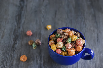 Multicolored sweet popcorn in  blue cup on gray wooden background.