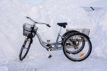 Three-wheeled bicycle in winter on a background of snowy hills, snowdrifts, fences and asphalt.