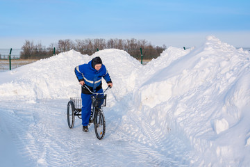 Cyclist in winter on a tricycle on a background of snowy hills, snowdrifts, fences and asphalt.The...