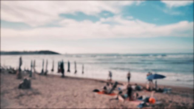 4k blured view of summer baech at Atlantic coast, Cantabrian sea, a lot of sunbathing people, colorful umbrellas, warm blue waves, orange sand and dramatic clouds on the sky