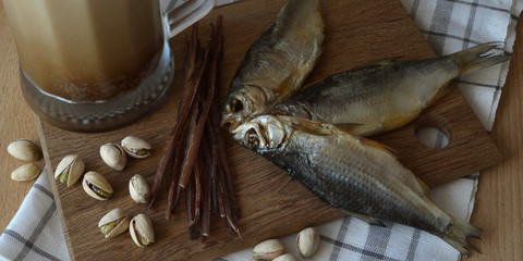 Three dried small fishes on a wooden board with a mug of beer, pistachios and a sea cobweb. Retro...