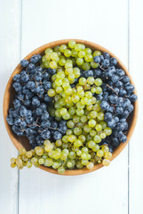 white and red grapes on wooden bowl, white wood table background