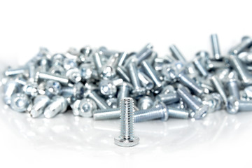 Single galvanized screw in front of a pile on white background