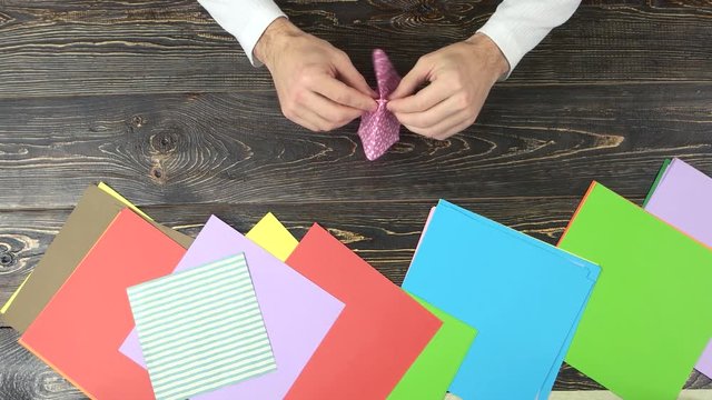 Hands making origami. Making rectangle from pink dotted paper, top view.