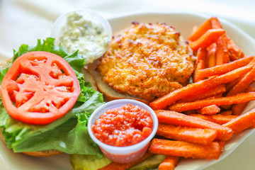 A hot, fresh, crab cake sandwich with tomato slices and sweet potato fries