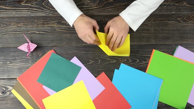 Hands making origami flower with yellow paper. Fast motion top view.