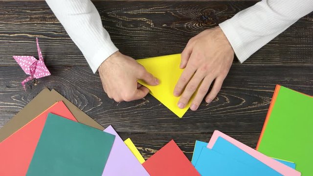 Male hands taking yellow paper. Making triangle with origami paper, top view.