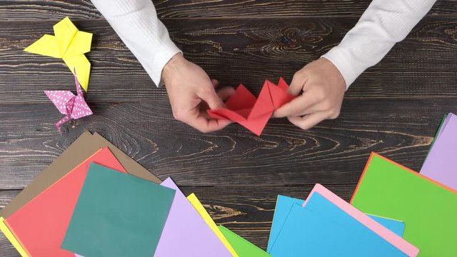 Making origami figure with red paper. Top view, male hands creating figure.
