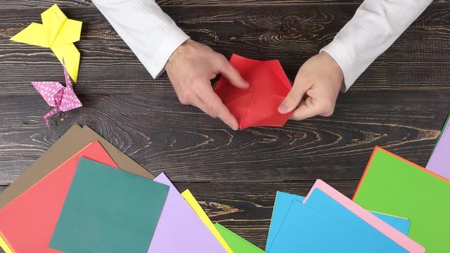 Hands making origami flower with red paper. Fast motion top view.