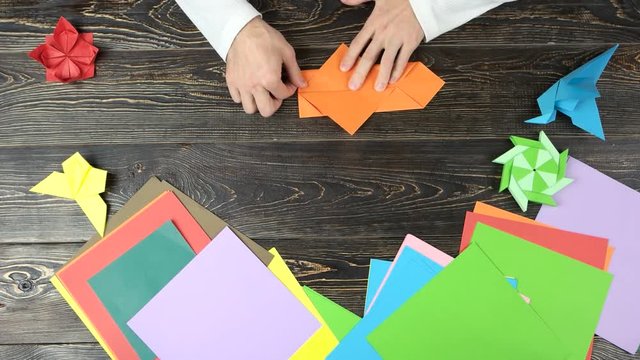 Making origami top view. Fast motion. Wooden desk surface background.