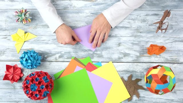 Making origami purple triangle. Wooden desk surface background.